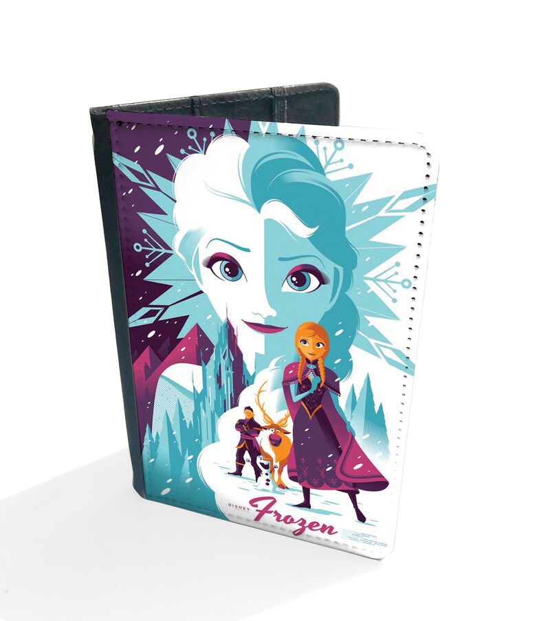 May include: A passport holder featuring a colorful illustration of Elsa and Anna from the Disney movie Frozen. The image shows the sisters standing in a snowy landscape with a castle in the background. The text "Frozen" is printed on the front of the holder.