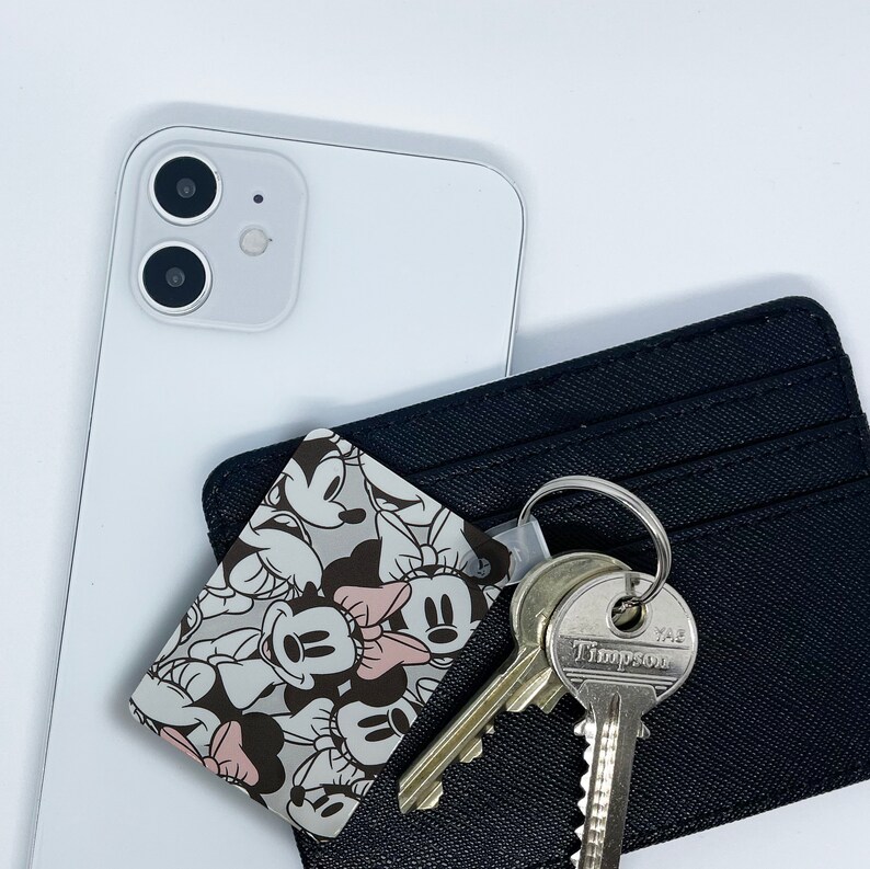 May include: A black leather wallet with a Mickey Mouse character print card holder. The card holder features a variety of Mickey Mouse characters in black and white. The wallet has a silver key chain with two keys attached. One key has the text "YALE" and the other key has the text "TIMPSON".