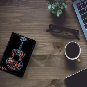 May include: A black leather notebook cover with a colorful illustration of a guitar with the word "Coco" on the front.