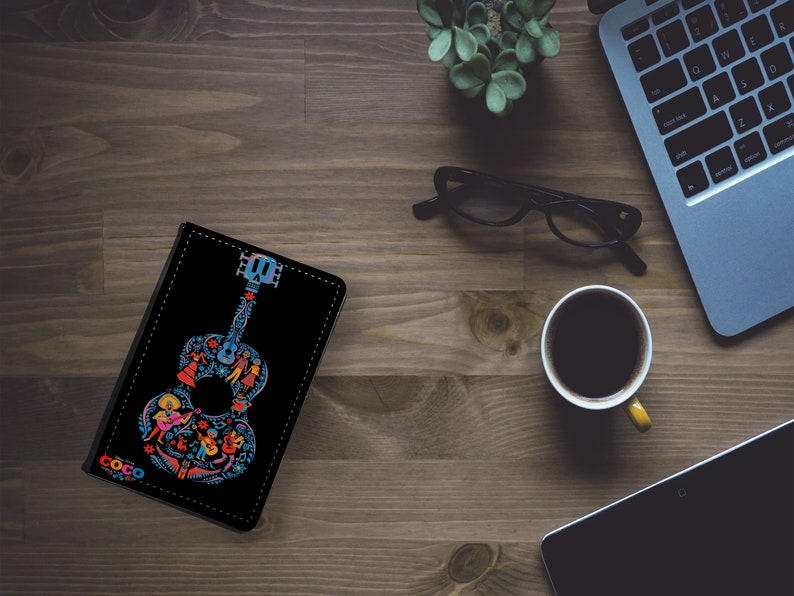 May include: A black leather notebook cover with a colorful illustration of a guitar with the word "Coco" on the front.