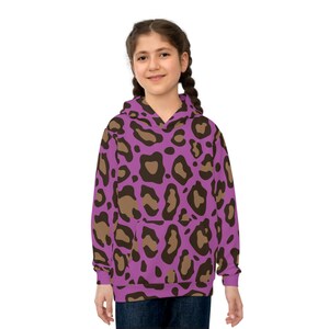 Può includere: Una felpa con cappuccio viola con un motivo leopardato marrone e beige. La felpa con cappuccio ha una tasca frontale e un cappuccio. La persona nella foto indossa jeans blu.