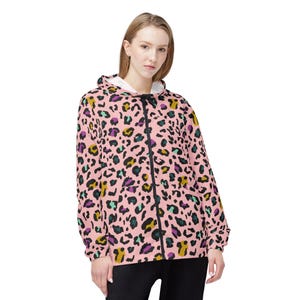 Peut inclure: Veste à capuche zippée rose avec un imprimé léopard coloré. La veste est dotée d'une fermeture éclair noire et d'une doublure intérieure blanche dans la capuche. Les taches de léopard sont dans les tons de noir, vert, jaune et violet.