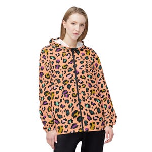 Peut inclure: Veste zippée pêche avec un imprimé léopard noir, vert, violet et jaune. La veste a une capuche et une fermeture éclair noire. Le modèle porte un pantalon noir.