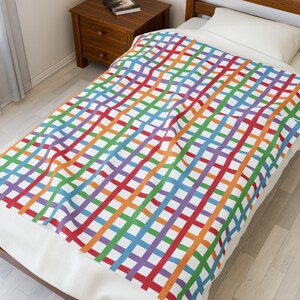 Può includere: Una coperta colorata con un vivace motivo a quadri a righe rosse, arancioni, verdi, blu e viola. La coperta è stesa su un letto, mostrando il suo design luminoso e la sua morbida consistenza. La coperta è un elemento di arredo per la casa.