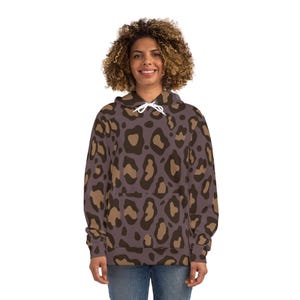 Può includere: Una felpa con cappuccio con un motivo leopardato marrone e beige. La felpa ha un cappuccio con coulisse e una tasca frontale. La modella indossa jeans blu.