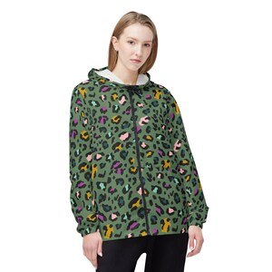 Peut inclure: Veste à capuche verte zippée avec un motif léopard coloré. La veste est dotée d'une fermeture éclair noire et d'une doublure intérieure blanche. Les taches de léopard sont dans les tons de rose, violet, jaune et noir.
