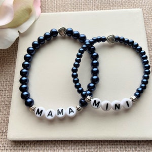 May include: Two beaded bracelets with silver heart charms. One bracelet says "MAMA" and the other says "MINI".
