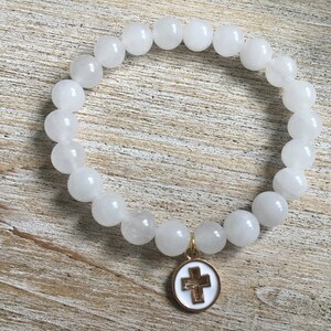 Op de afbeelding: Witte kralenarmband met een goudkleurige kruisbedel. De armband heeft ronde, ondoorzichtige witte kralen. De bedel is een wit ge&euml;mailleerd kruis met een goudkleurige rand en een goudkleurige balein.