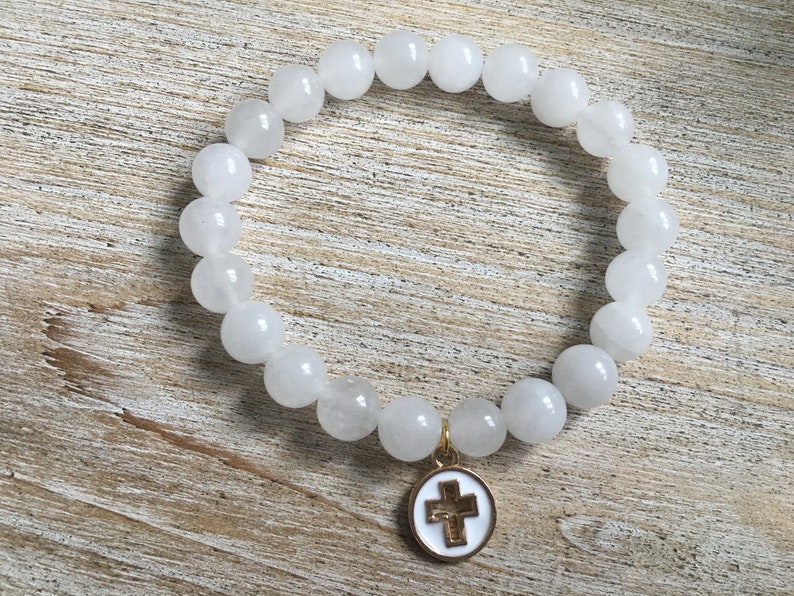 Op de afbeelding: Witte kralenarmband met een goudkleurige kruisbedel. De armband heeft ronde, ondoorzichtige witte kralen. De bedel is een wit ge&euml;mailleerd kruis met een goudkleurige rand en een goudkleurige balein.