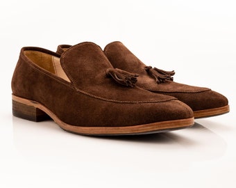 Può includere: Mocassini in pelle scamosciata marrone con nappine e suola in pelle. I mocassini hanno una punta a punta e un design slip-on.