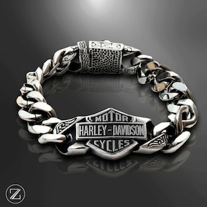 Peut inclure: Un bracelet à chaîne en métal argenté doté d'un emblème central en forme de bouclier avec le texte en relief MOTOR HARLEY-DAVIDSON CYCLES. Le bracelet se compose de maillons épais et imbriqués et d'un fermoir rectangulaire texturé.