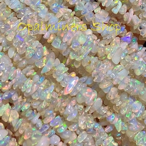 Puede incluir: Una hebra de cuentas de chip de ópalo blanco con destellos iridiscentes de arcoíris. Las cuentas son de forma y tamaño irregulares, y están enhebradas en un hilo transparente.