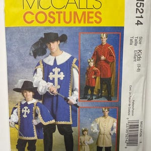 May include: A McCall's Costumes sewing pattern envelope M5214 for kids sizes 3-8. The front displays three historical costume variations: a blue tunic with a cross, a red tunic with a cape, and a tan tunic, all featuring crowns and swords.
