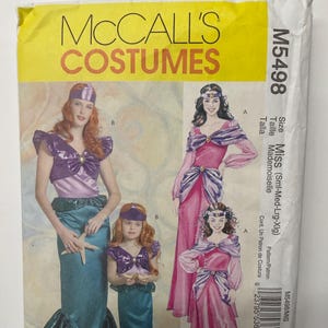 May include: McCall's Costumes M5498 sewing pattern envelope featuring illustrations of two costume styles: a mermaid outfit with a teal skirt and purple top, and a long pink gown with purple accents. The text includes size Miss Sml-Med-Lrg-Xlg.
