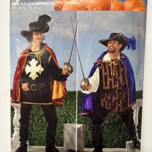 May include: Simplicity 0815 Halloween sewing pattern envelope featuring two costume variations. One shows a black tunic with a gold cross and red cape, the other a striped tunic with a blue cape. Both include hats with feathers and swords.