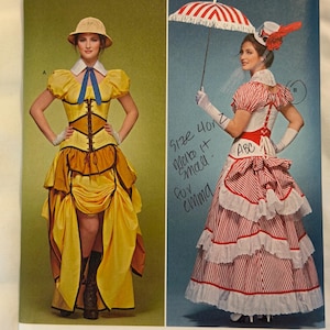 May include: Simplicity sewing pattern 8159 featuring two costume designs. The left shows a yellow dress with a brown corset and pith helmet. The right shows a red and white striped dress with a matching parasol and hat. Handwritten notes are present.