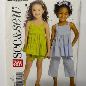 May include: A See & Sew B5009 sewing pattern envelope featuring two outfits. One is a lime green floral print tiered tank top with matching shorts. The other is a blue and white pinstriped tiered tank top with matching cropped pants.