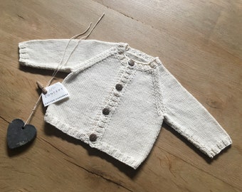 May include: A white knitted baby cardigan with button fastenings. The cardigan has a tag that reads "Concept Cotton & Cashmere".
