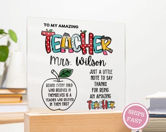 May include: A clear acrylic plaque with the words "TO MY AMAZING TEACHER" in colorful letters. The name "Mrs. Wilson" is below the title. The plaque includes an apple graphic and the text "BEHIND EVERY CHILD WHO BELIEVES IN THEMSELVES IS A TEACHER WHO BELIEVED IN THEM FIRST."