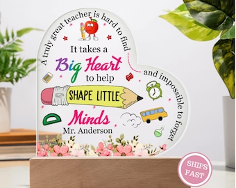 May include: A heart-shaped acrylic plaque with a wooden base, featuring the text "It takes a Big Heart to help Shape Little Minds." The design includes illustrations of a pencil, apple, school bus, and flowers. The name "Mr. Anderson" is also included.