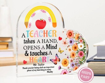 May include: A heart-shaped acrylic plaque with a colorful design for a teacher. The plaque features a rainbow, apple, and floral arrangement. Text reads: "A TEACHER takes A HAND, OPENS A Mind & touches A HEART." Includes the text "SHIPS FAST."