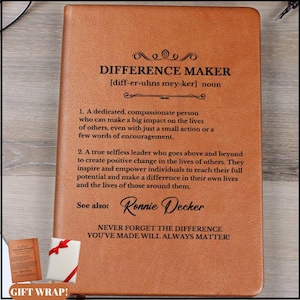 May include: A tan leather journal with the words "DIFFERENCE MAKER" embossed on the cover. The definition of "Difference Maker" is printed below, along with the name "Ronnie Decker" and the phrase "NEVER FORGET THE DIFFERENCE YOU'VE MADE WILL ALWAYS MATTER!"