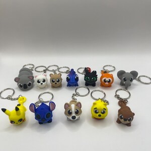 May include: A set of 12 colorful cartoon character keychains. The keychains feature characters like Stitch, Pikachu, a koala, a cat, and a dog. The keychains are made of a soft, rubbery material and are perfect for adding a touch of fun to your keys or bag.