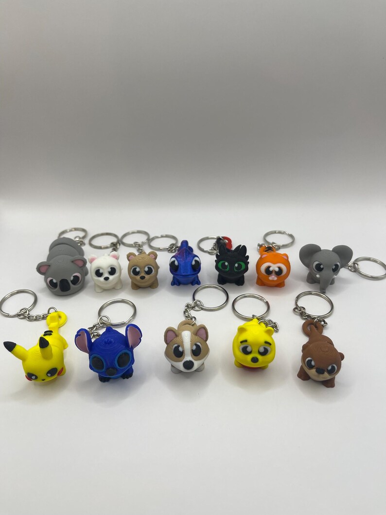 May include: A set of 12 colorful cartoon character keychains. The keychains feature characters like Stitch, Pikachu, a koala, a cat, and a dog. The keychains are made of a soft, rubbery material and are perfect for adding a touch of fun to your keys or bag.