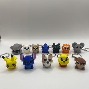 May include: A collection of 12 colorful cartoon character keychains. The keychains feature characters like Stitch, Winnie the Pooh, Pikachu, and a koala.
