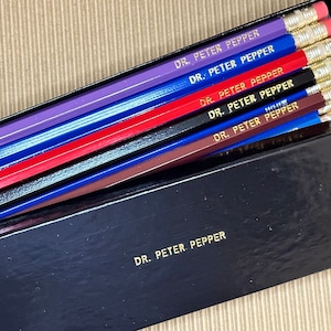 May include: A box of Dr. Pepper pencils in a variety of colors, including purple, blue, red, black, and brown. The pencils are all sharpened and ready to use.