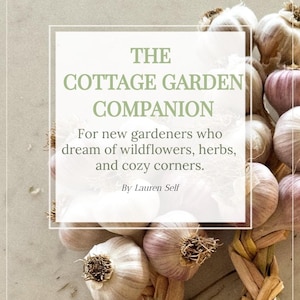 May include: A book cover titled "The Cottage Garden Companion" with text about gardening. The image features a bundle of garlic bulbs, some with purple hues, and a woven garlic braid.