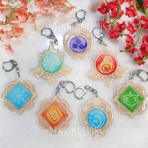 May include: Seven keychains with different colored and patterned designs. Each keychain features a different symbol in the center, including a snowflake, a heart, a flame, a swirl, and a crescent moon. The keychains are made of clear acrylic and have a gold-colored metal ring.
