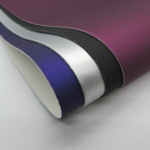May include: A stack of five fabric swatches in different colors. The swatches are arranged in a fan shape, with the top swatch being a deep purple, followed by black, silver, blue, and white.