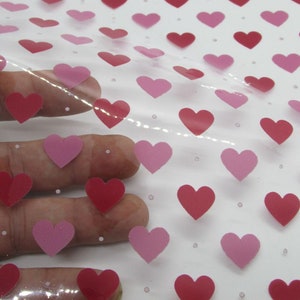 May include: Clear plastic sheet with a repeating pattern of pink and red hearts. The sheet is slightly translucent and has a subtle shimmer.