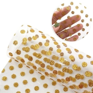May include: Clear vinyl sheet with gold glitter polka dots. The sheet is translucent and the dots are scattered randomly across the surface.