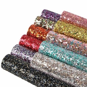 May include: A collection of rolled glitter fabric in various colors, including black, silver, teal, pink, gold, orange, red, and purple. The glitter is densely packed, creating a sparkling effect. The rolls are stacked, showcasing the range of colors.