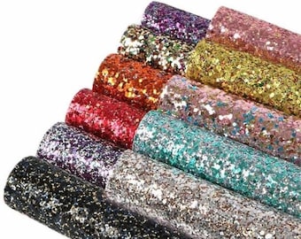May include: A collection of rolled glitter fabric in various colors, including black, silver, teal, pink, gold, orange, red, and purple. The glitter is densely packed, creating a sparkling effect. The rolls are stacked, showcasing the range of colors.