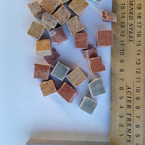 May include: A collection of small, square mosaic tiles in shades of brown, red, and green are scattered on a white surface. A wooden ruler with metric and imperial measurements is positioned next to the tiles. The ruler is marked with the text "HARDENED STEEL" and "ACIER TREMPE".