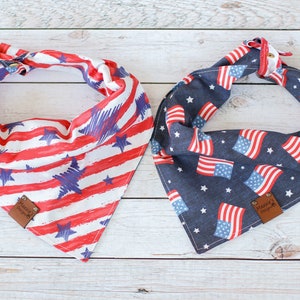 May include: Two patriotic dog bandanas, one with red and white stripes and blue stars, and the other with blue fabric and red, white, and blue stars. Both bandanas have a brown leather tag with "Happy Dog Days" printed on them.