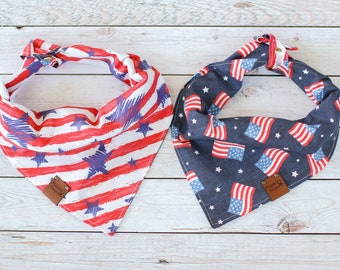 Puede incluir: Dos bandanas patrióticas para perros, una con rayas rojas y blancas y estrellas azules, y la otra con tela azul y estrellas rojas, blancas y azules. Ambas bandanas tienen una etiqueta de cuero marrón con "Happy Dog Days" impreso en ellas.
