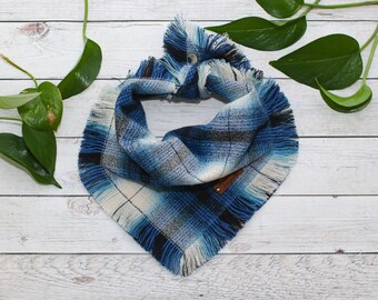 May include: A blue and white plaid dog bandana with frayed edges. The bandana has a brown leather tag with the word "Doggy" on it.