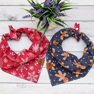 May include: Two festive dog bandanas, one red with white snowflakes and the other navy blue with gingerbread men. Both bandanas have a brown leather tag with the word "Handmade" on it.