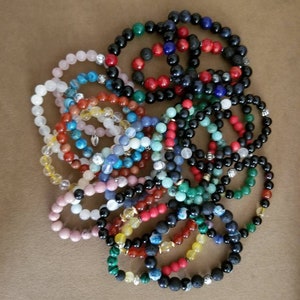 Puede incluir: Una colección de pulseras de cuentas coloridas con varias piedras y dijes. Las pulseras están hechas con roca de lava negra, ágata, turquesa y otras piedras naturales.