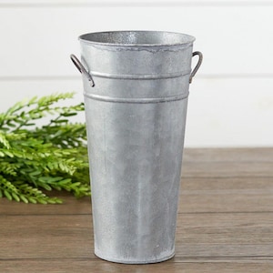 May include: A tall, galvanized metal vase with two small handles. The vase has a cylindrical shape and a slightly distressed finish. The vase is suitable for displaying flowers or other decorative items.