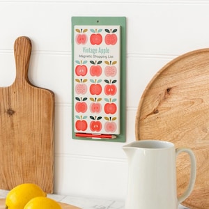May include: A rectangular magnetic shopping list with a green backing, featuring a repeating pattern of red and pink apples. The text "Vintage Apple Magnetic Shopping List" is printed on the list. A red pencil is included. Kitchen-themed.