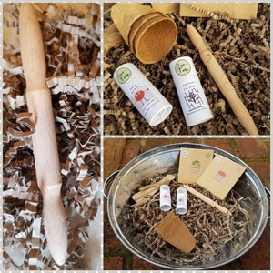 May include: A gardening kit containing a wooden trowel, seed paper, and biodegradable pots. The kit is presented in a metal bucket with brown paper shredding. The seed paper has the text "Seed Tape" and "Wild Flower Mix" printed on it.