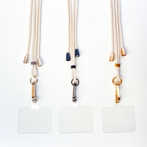 K&ouml;nnte beinhalten: Drei wei&szlig;e Lanyardschnurrb&auml;nder mit verschiedenen farbigen Metallakzenten und durchsichtigen Plastik-Ausweishaltern.