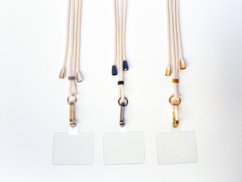 K&ouml;nnte beinhalten: Drei wei&szlig;e Lanyardschnurrb&auml;nder mit verschiedenen farbigen Metallakzenten und durchsichtigen Plastik-Ausweishaltern.