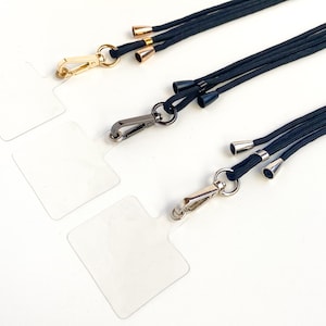 K&ouml;nnte beinhalten: Drei schwarze Lanyards mit verschiedenen Metallverschl&uuml;ssen und dekorativen Spitzen. Die Lanyards bestehen aus geflochtenem Kordel und haben eine goldene, silberne und schwarze Oberfl&auml;che.