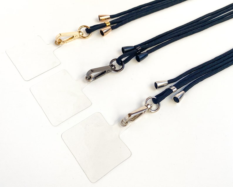 K&ouml;nnte beinhalten: Drei schwarze Lanyards mit verschiedenen Metallverschl&uuml;ssen und dekorativen Spitzen. Die Lanyards bestehen aus geflochtenem Kordel und haben eine goldene, silberne und schwarze Oberfl&auml;che.